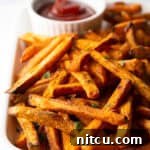 Piles of cooked sweet potatoes on a large serving pan with a white ramekin of ketchup.