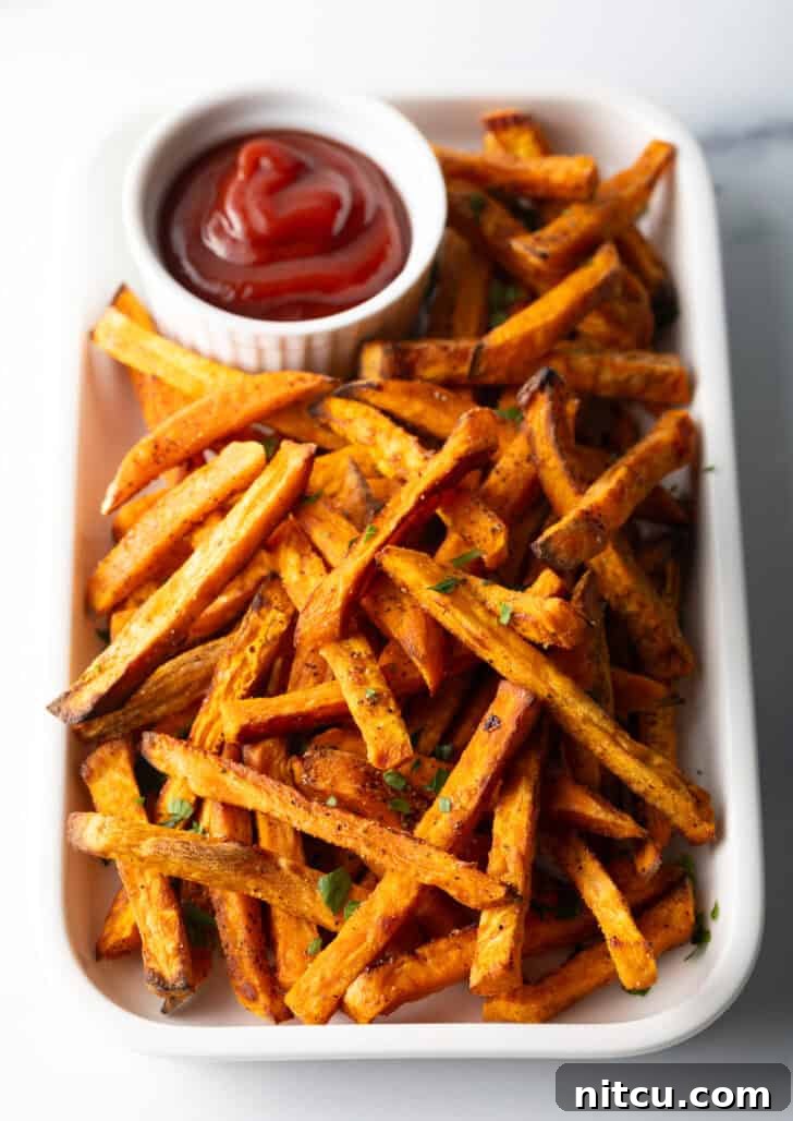 Crispy Air Fryer Sweet Potato Fries 4 Piles of cooked air fryer or baked sweet potatoes on a large serving pan with a white ramekin of ketchup.