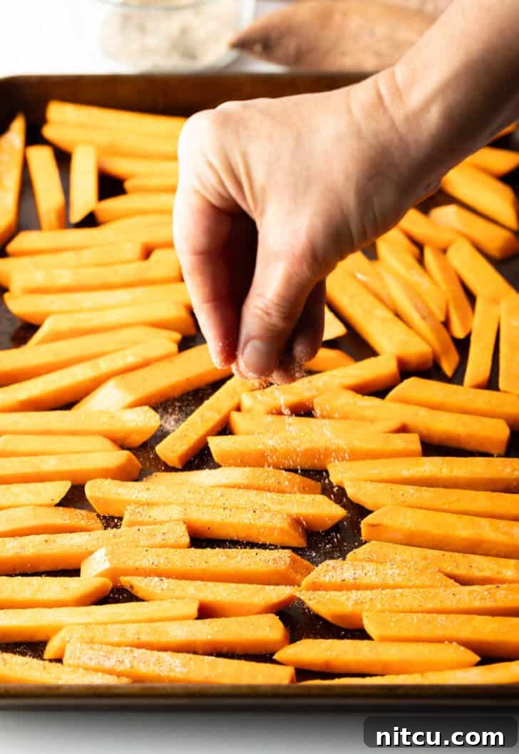 Crispy Air Fryer Sweet Potato Fries 7 Hand placing raw slices of potatoes on a baking sheet.