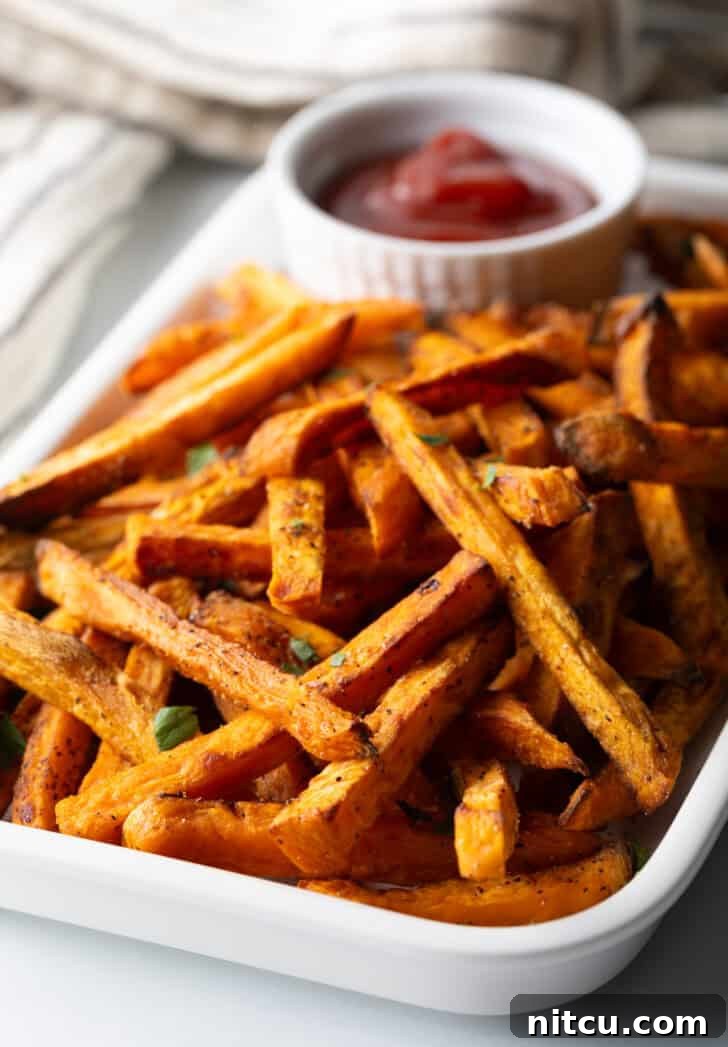 Crispy Air Fryer Sweet Potato Fries 10 Piles of cooked baked or air fryer sweet potatoes on a large serving pan with a white ramekin of ketchup.