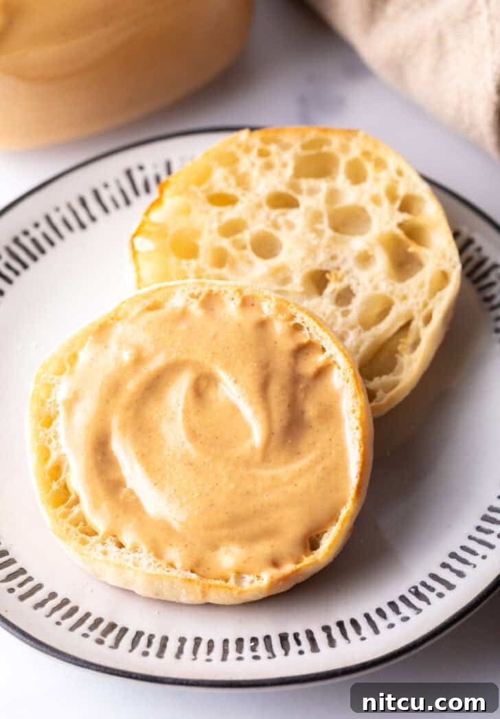 Whip Up Your Own Peanut Butter 13 An open English muffin on a plate, with one half generously covered in smooth homemade peanut butter.