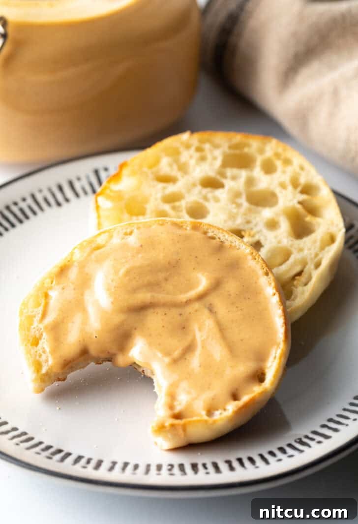 Whip Up Your Own Peanut Butter 14 An open English muffin on a plate, one half covered with homemade peanut butter and a bite taken out, showing its creamy texture.