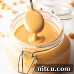 Whip Up Your Own Peanut Butter 15 A spoon taking a scoop of peanut butter from a glass jar, showing the butter to camera.