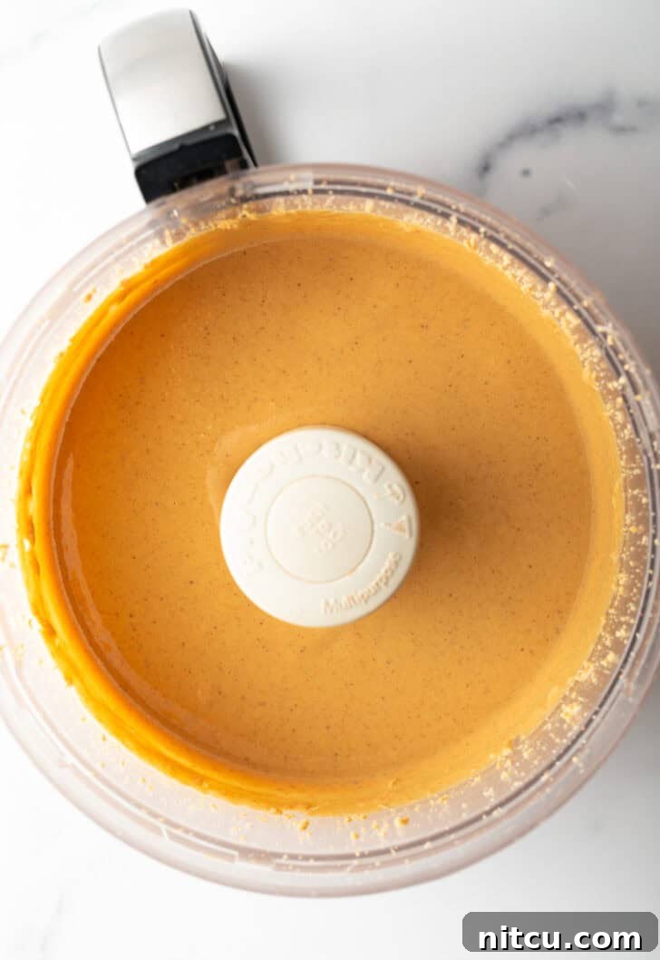 Whip Up Your Own Peanut Butter 10 Smooth, glossy peanut butter swirling in the food processor, indicating it's nearly ready.