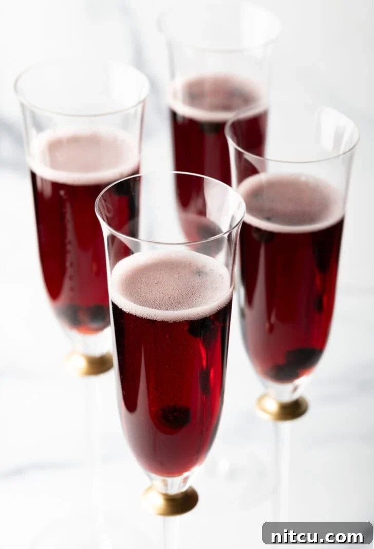 Regal Berry Fizz 4 Another perspective of four fluted glasses filled with rich red Kir Royale cocktails.