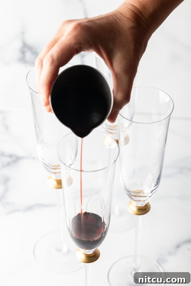 Regal Berry Fizz 6 A hand carefully pouring deep red crème de cassis into a champagne flute.
