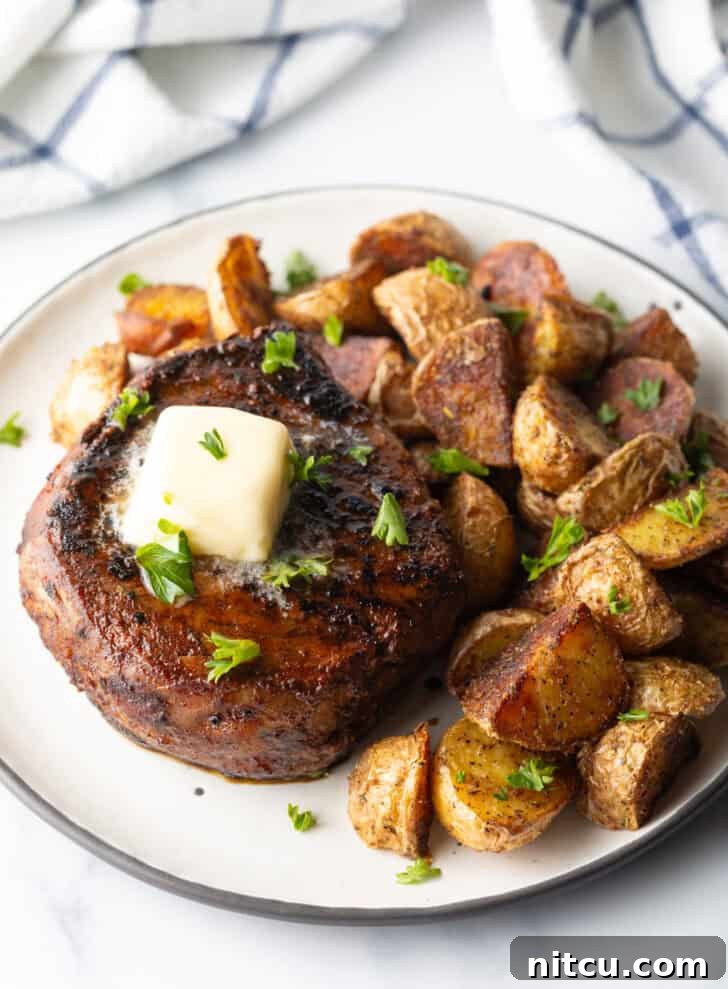 Achieve Steakhouse Quality with Reverse Searing 3 White plate with a reverse sear steak, topped with chopped herbs and a pat of butter. Roasted yellow potato pieces are on the right side of the meat.