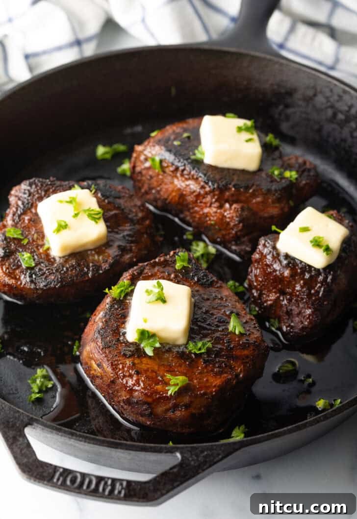 Achieve Steakhouse Quality with Reverse Searing 4 Four filets searing in a cast iron skillet. Each steak is topped with fresh chopped herbs and a pat of butter.