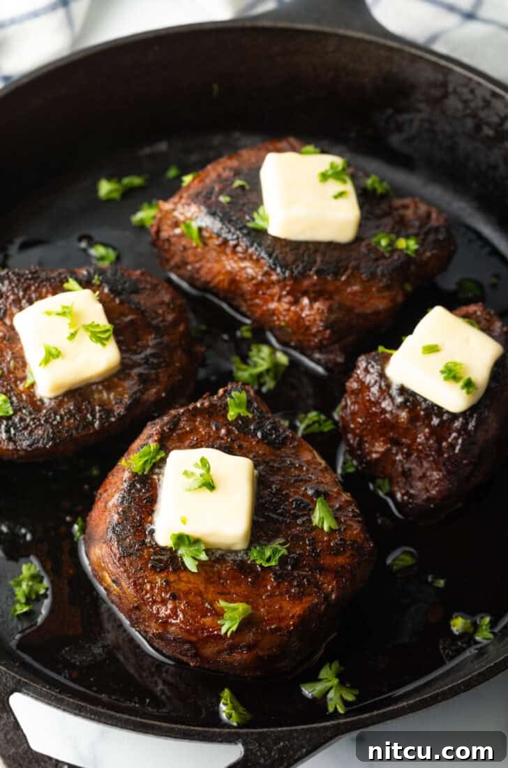Achieve Steakhouse Quality with Reverse Searing 7 Four filets searing in a cast iron skillet. Each steak is topped with fresh chopped herbs and a pat of butter.