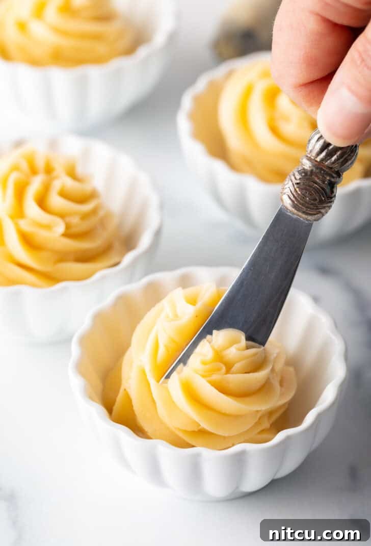 Butter knife gently spreading a swirl of golden whipped honey butter in a small white ramekin, showcasing its creamy texture.