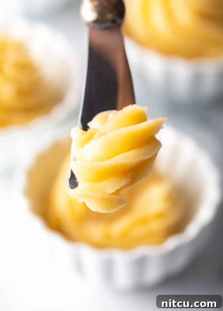 A close-up shot of a butter knife expertly cutting into a rich swirl of golden whipped honey butter, resting in a pristine white ramekin.