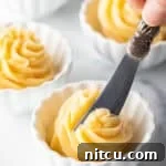 A close-up of a butter knife cutting into a swirling, fluffy mound of whipped honey butter in a small ramekin, emphasizing its creamy texture.