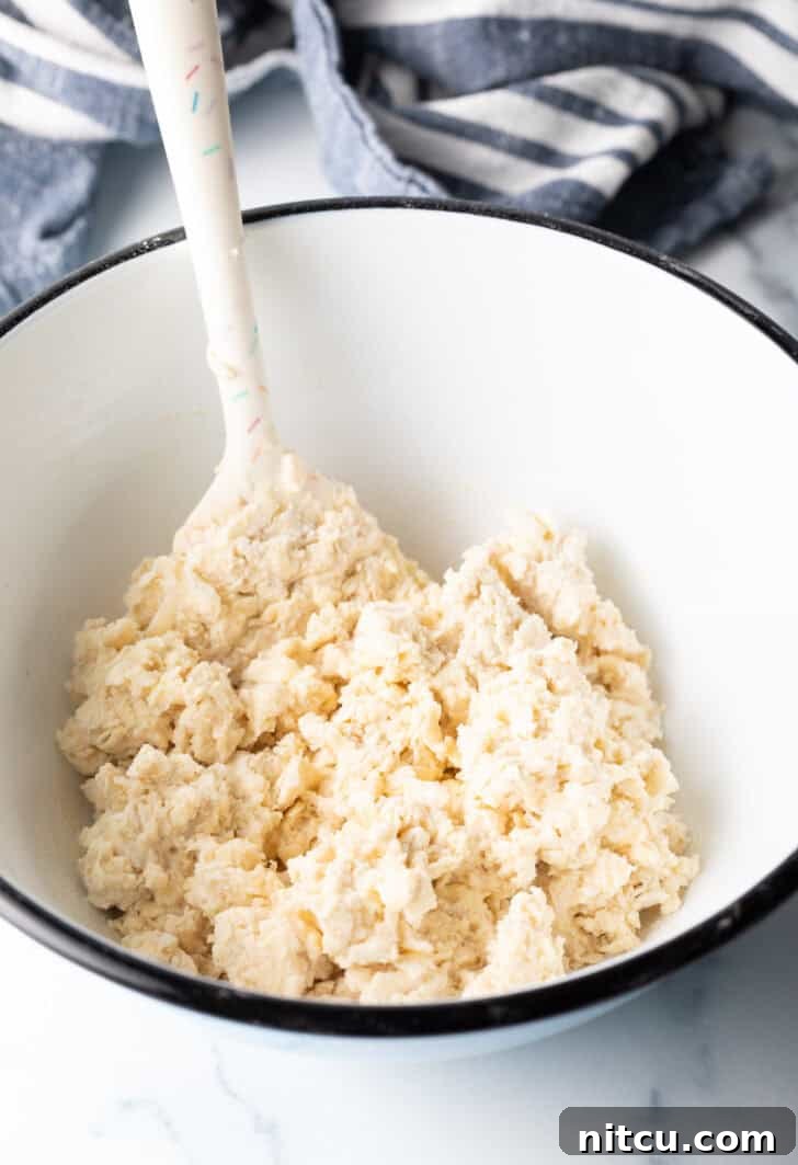 Pillowy Buttermilk Drop Biscuits 8 Sticky dough in a white bowl being stirred by a white spatula.