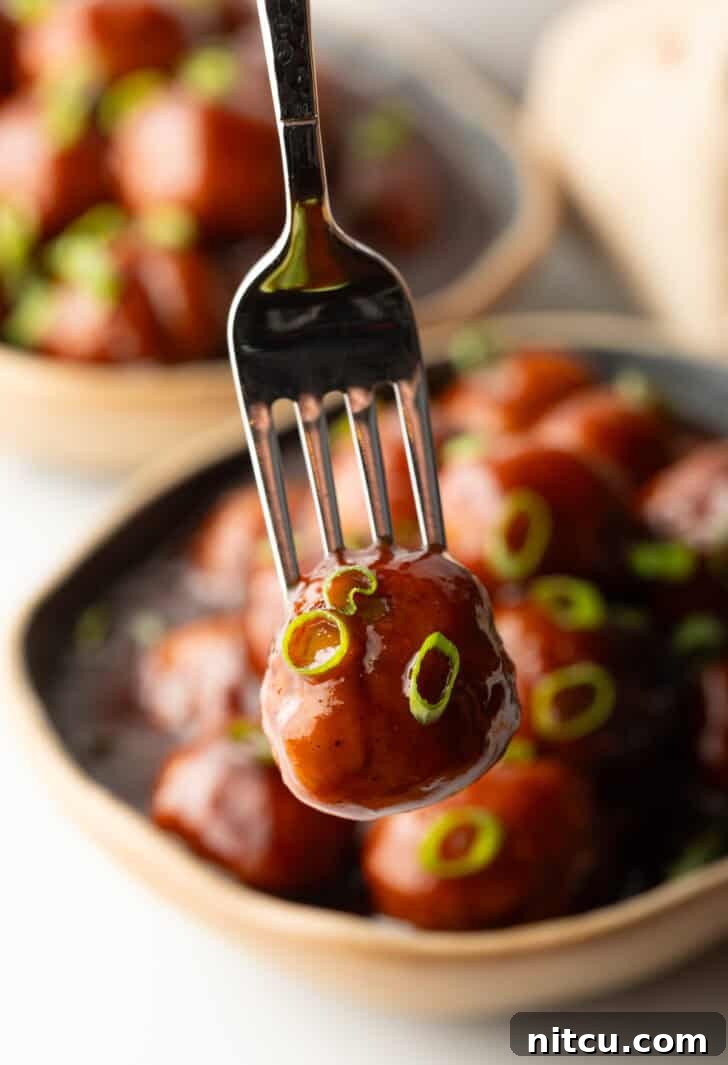 Sweet & Smoky Slow Cooker Meatballs 10 A fork is holding a bbq sauce-coated meatball to camera.