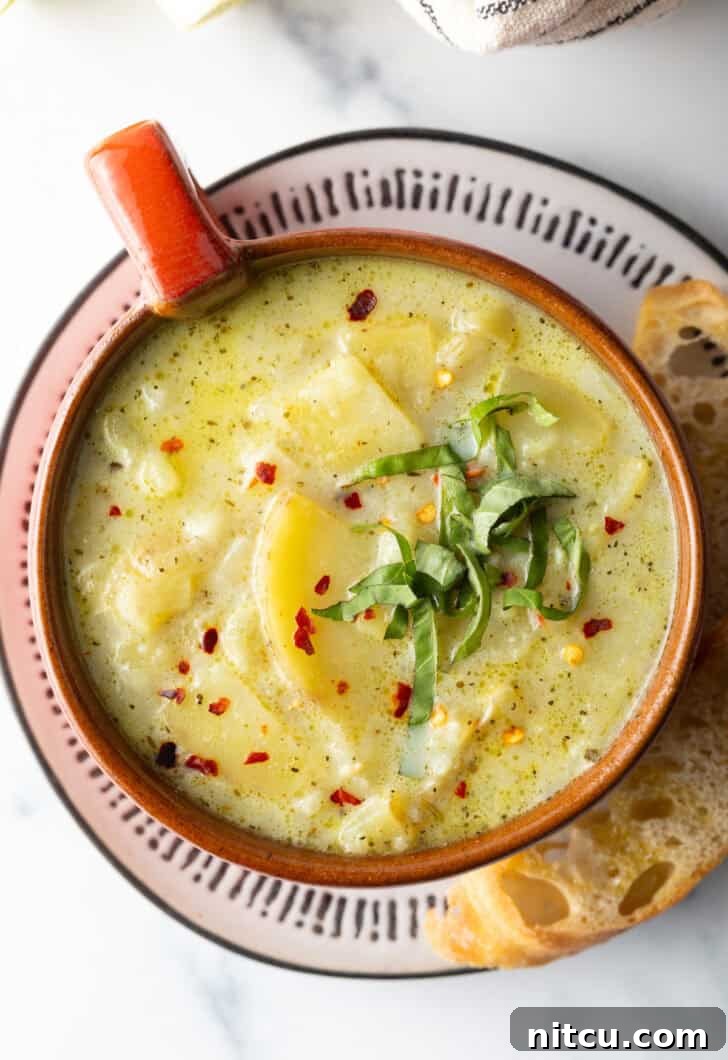 Top down view of an oversized mug filled with potato leek soup, on a plate with slice of baguette on the side.