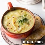 Red oversized mug filled with leek and potato soup, on a plate with slice of baguette on the side.