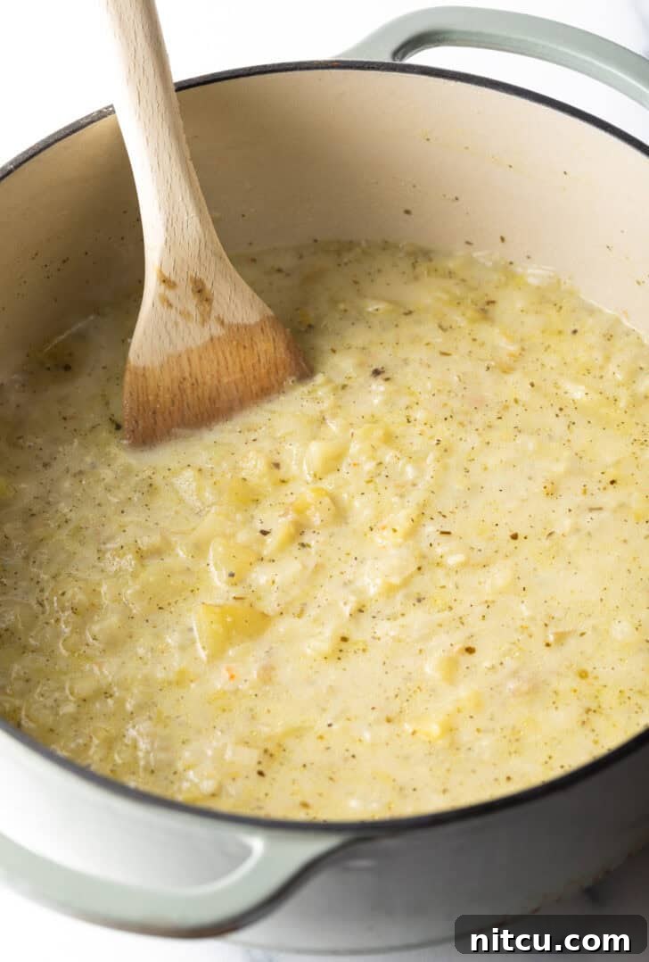 Wood spoon stirring a creamy batch of soup in a large pot.