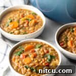 Classic Homestyle Lentil Soup 13 Three white bowls of lentil soup with carrots and kale.