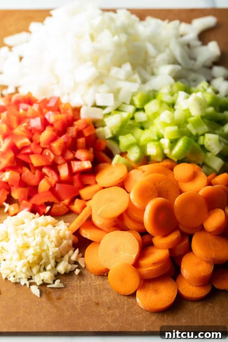 Classic Homestyle Lentil Soup 5 Finely chopped fresh ingredients, including vibrant onion, red peppers, sweet carrots, pungent garlic, and crisp celery, arranged neatly on a rustic wood cutting board, ready for soup preparation.