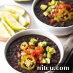 Hearty Black Bean Soup 9 Two white bowls of black bean soup topped with slices of jalapenos, chopped avocado, and pico de gallo.