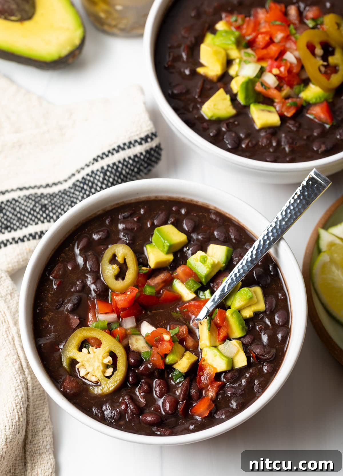 Hearty Black Bean Soup 3 White bowl of black bean soup topped with slices of jalapenos, chopped avocado, and pico de gallo.