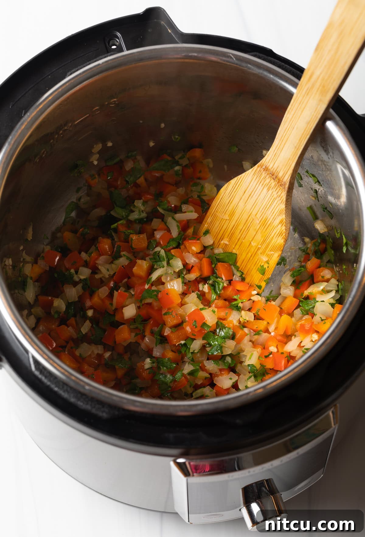 Hearty Black Bean Soup 5 Sauteed red peppers and onions in an instant pot with a wooden spatula.