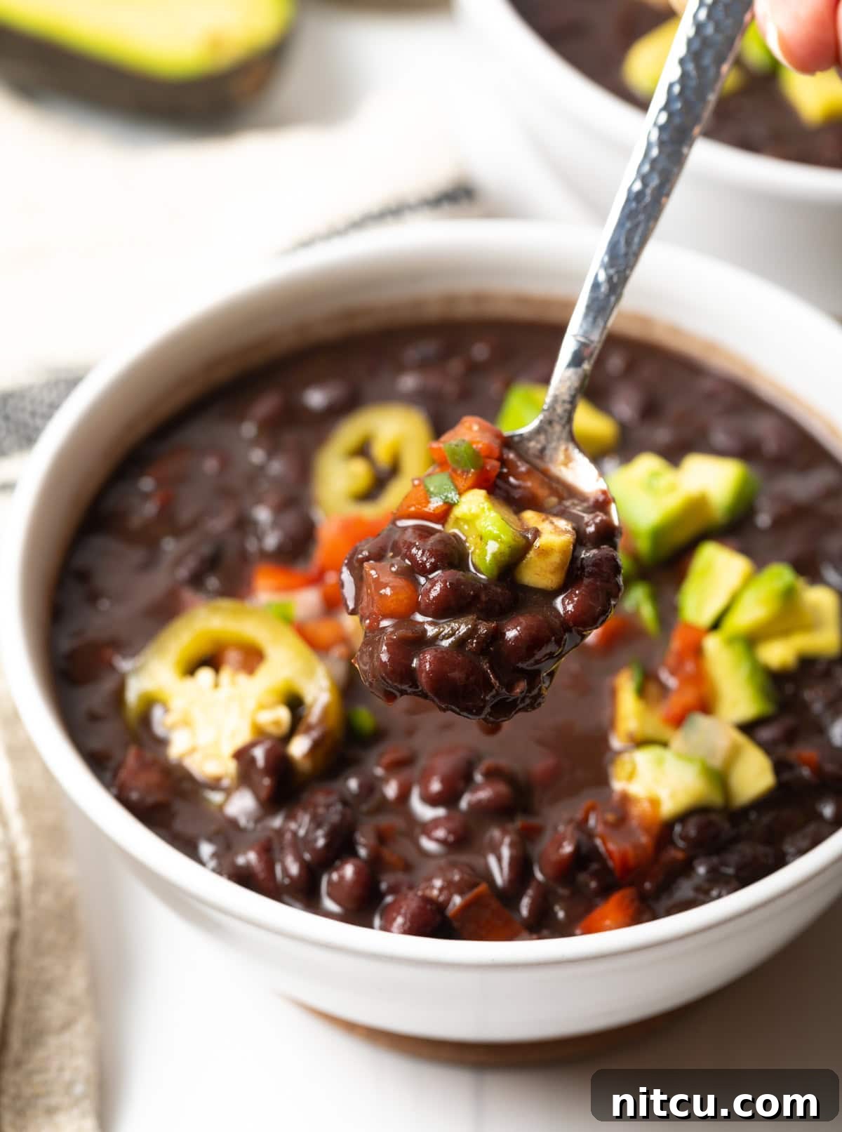 Hearty Black Bean Soup 8 White bowl of black bean soup topped with slices of jalapenos, chopped avocado, and pico de gallo.