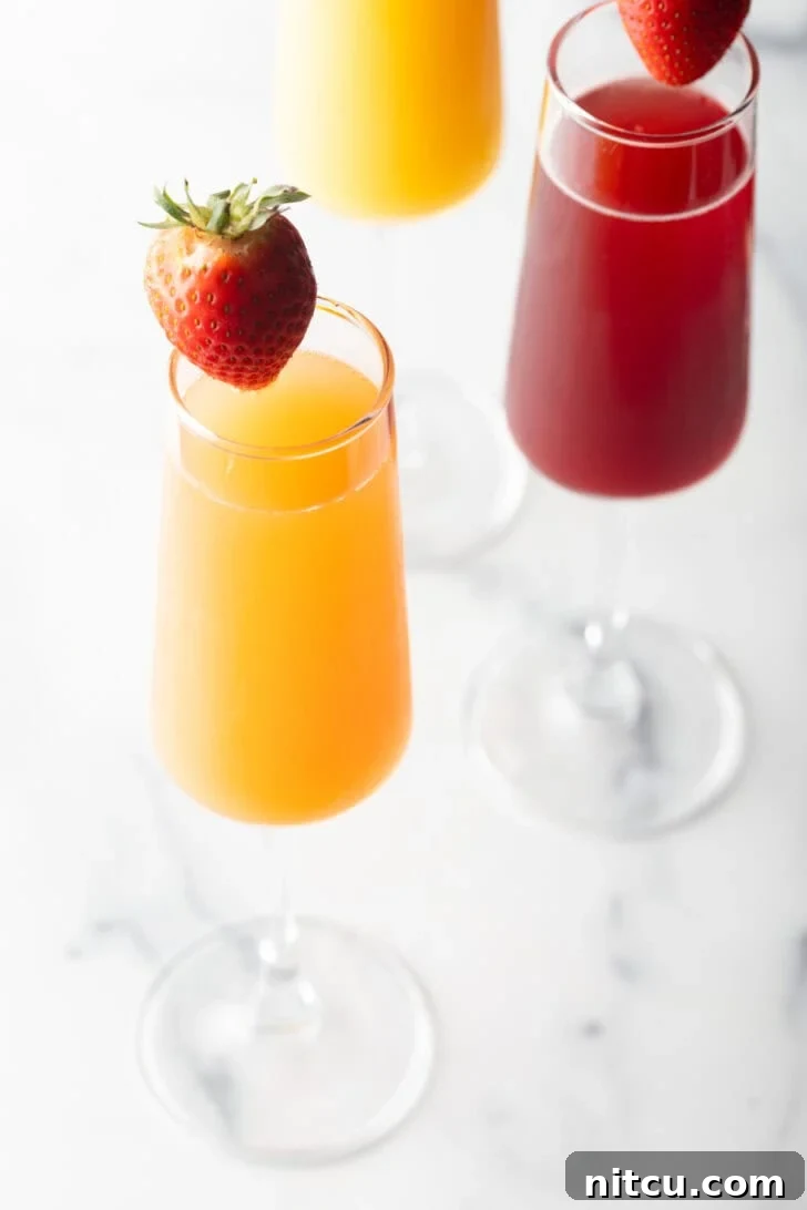 The Ultimate Mimosa Recipe 11 A champagne flute filled with orange mimosa, and another glass filled with a cranberry mimosa. Both glasses are garnished with a whole strawberry on the rim.