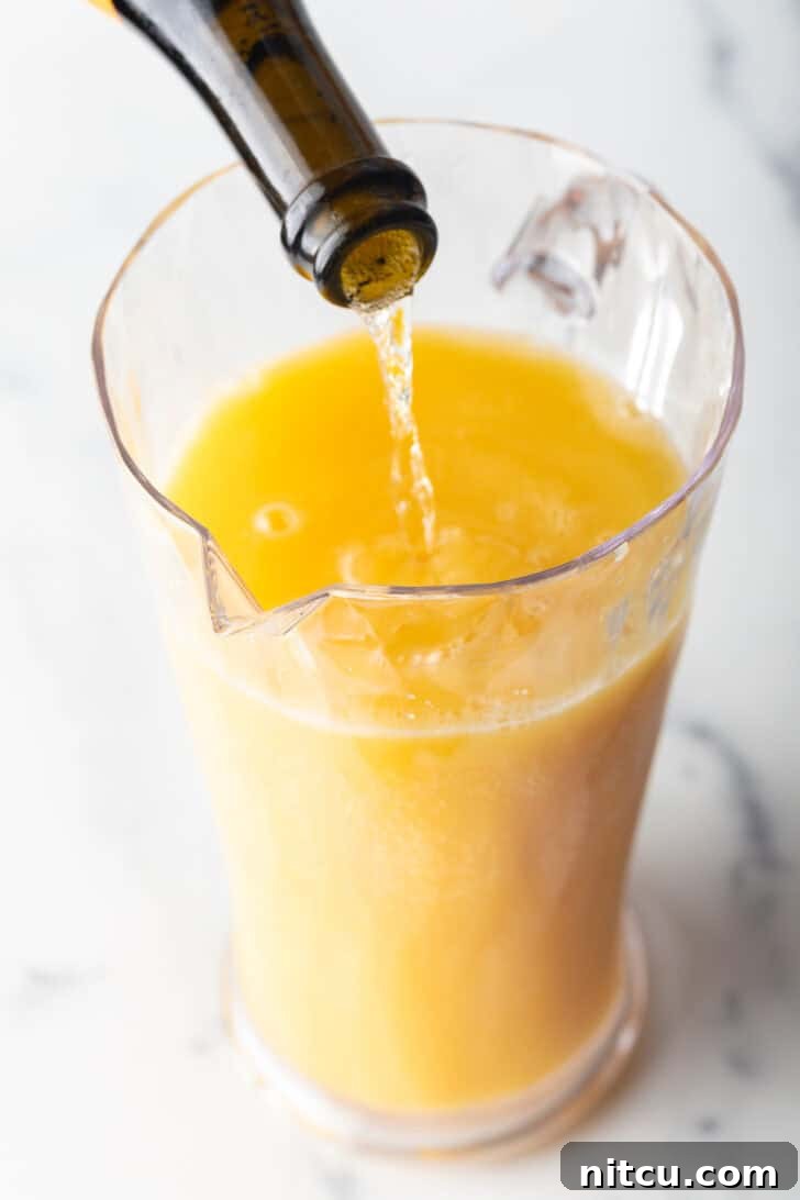The Ultimate Mimosa Recipe 6 Pouring sparkling wine form the bottle into a glass pitcher with orange juice.