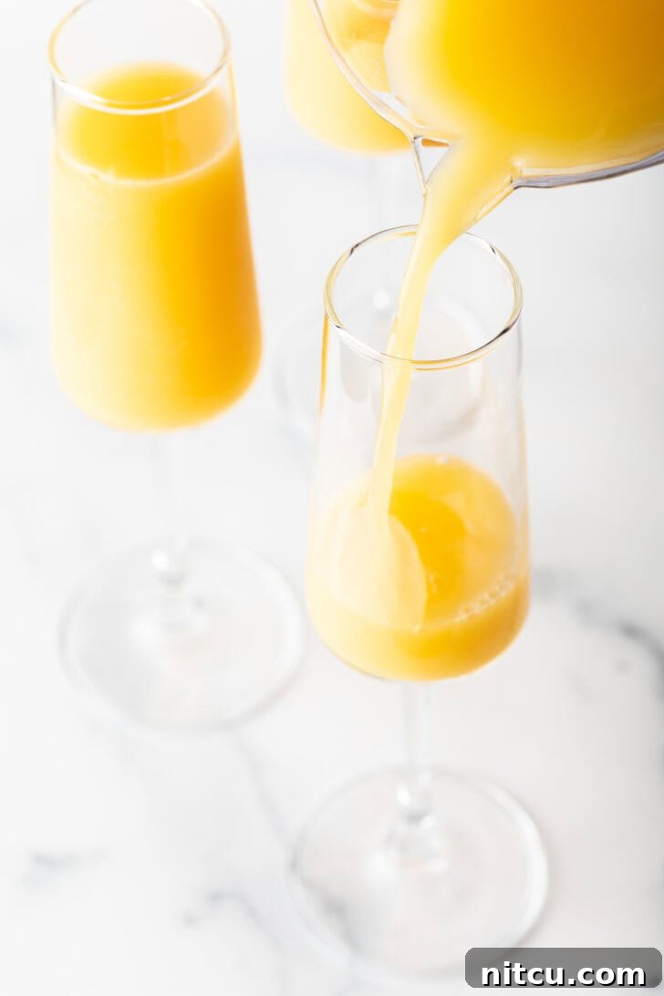The Ultimate Mimosa Recipe 7 Pouring orange juice from a pitcher into a tall champagne glass.