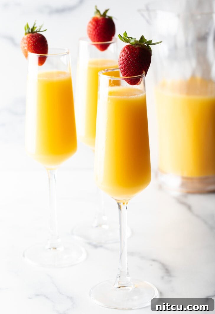 The Ultimate Mimosa Recipe 9 3 champagne glasses full of mimosa and each garnished with a whole strawberry on the rim.