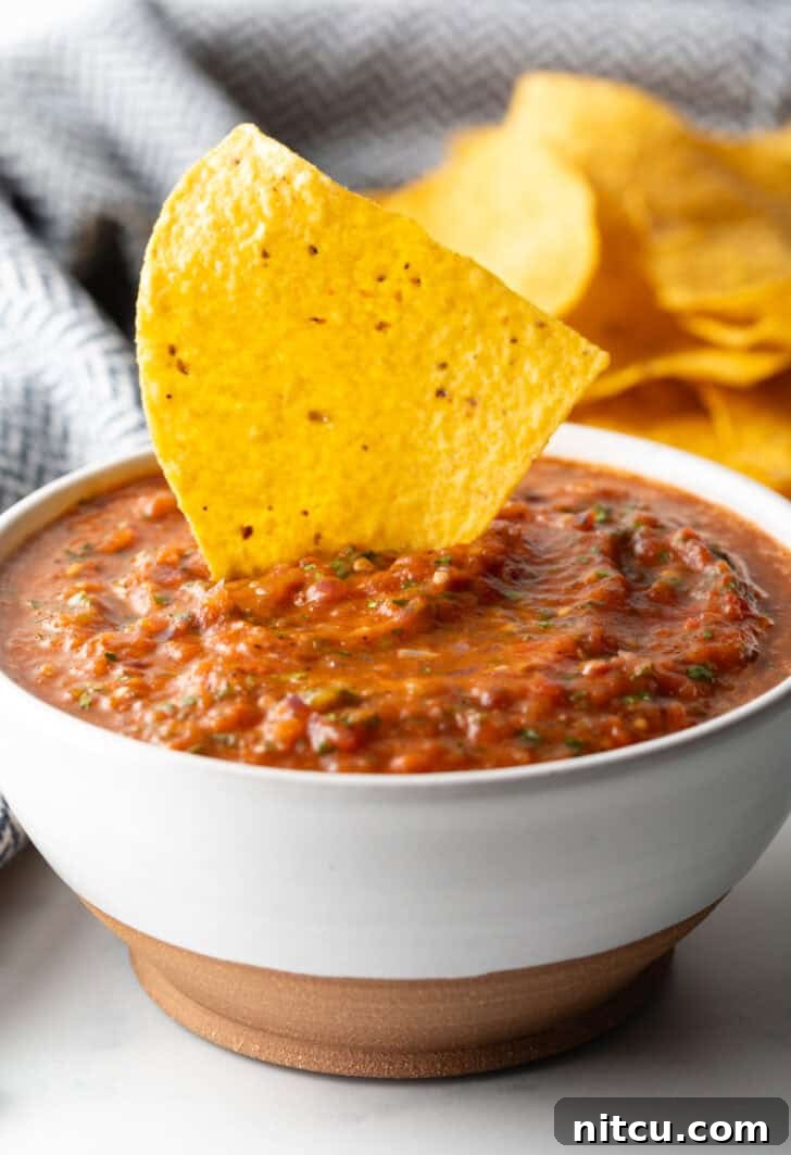Charred Tomato Salsa 4 White bowl of roasted tomato salsa. A tortilla chip is sticking out of the salsa.