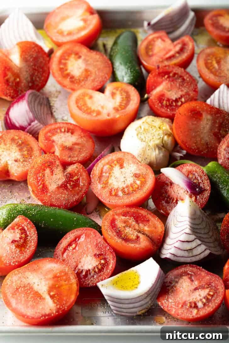 Charred Tomato Salsa 6 Top down view baking sheet brimming with fresh raw sliced tomatoes, jalapeno, and red onion chunks.