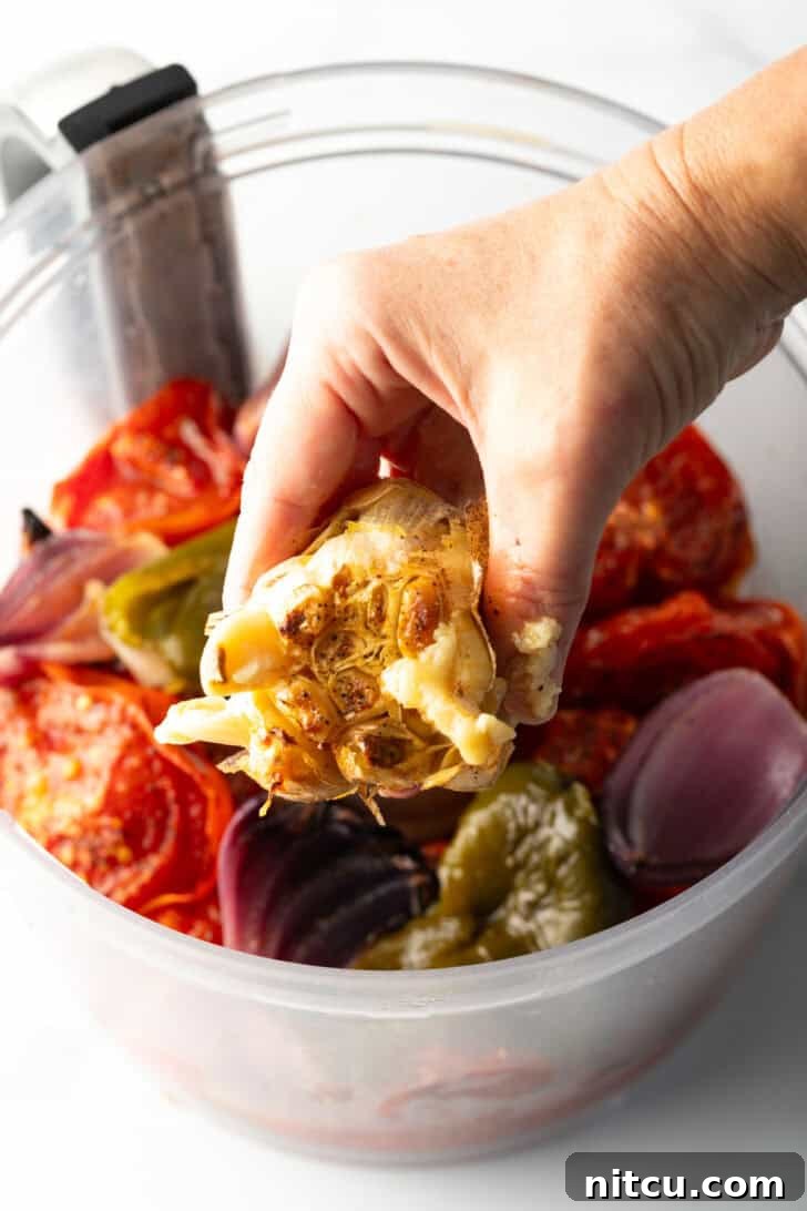 Charred Tomato Salsa 8 Hand squeezing roasted garlic into a food processor with other salsa ingredients.