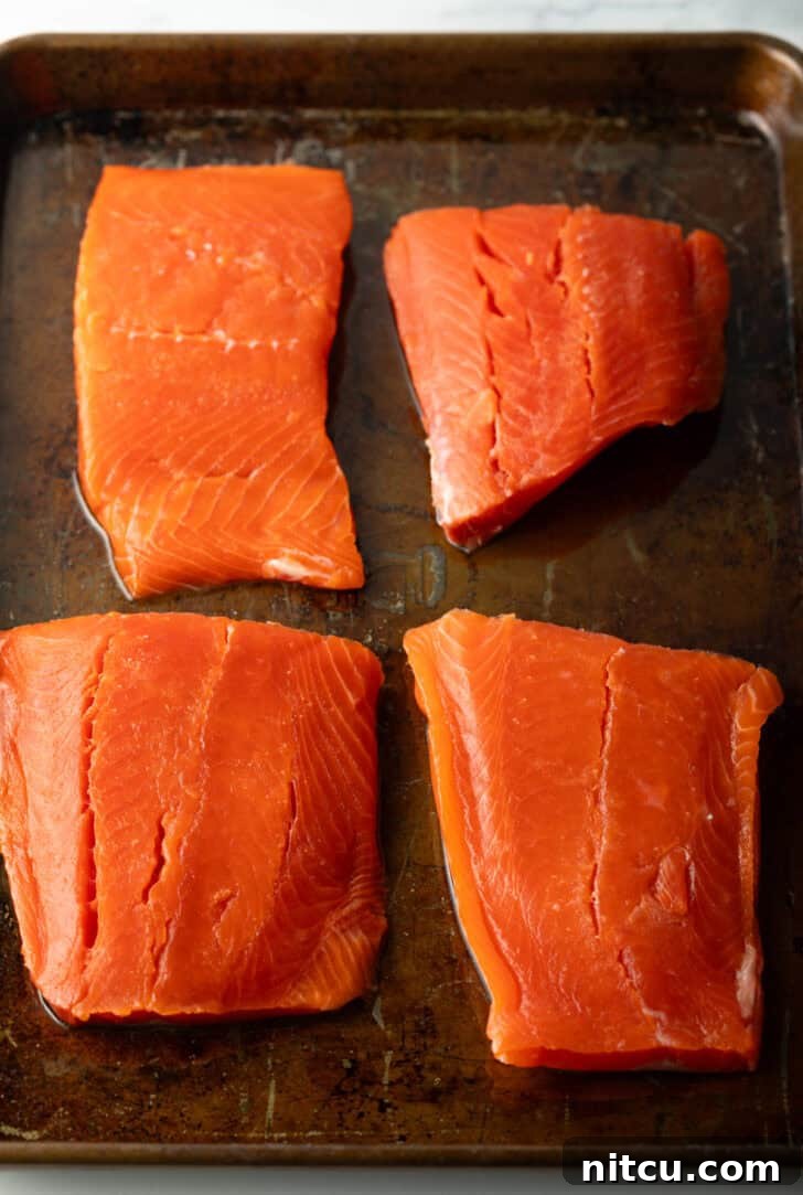 Perfect Oven-Baked Salmon 5 4 raw pieces of salmon filets on a baking sheet.