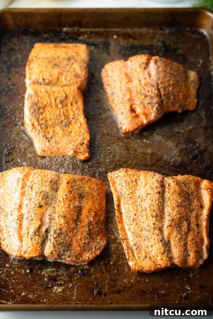 Perfect Oven-Baked Salmon 8 4 baked seasoned filets of salmon on a baking sheet.
