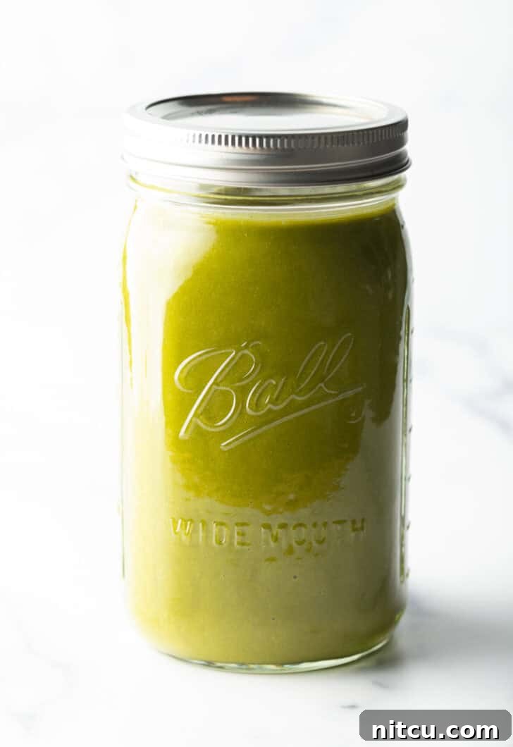 Another view of a large glass mason jar filled with bright green enchilada sauce.