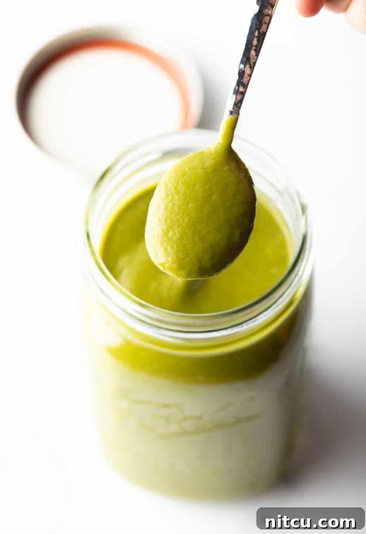 A spoonful of smooth, vibrant green poblano sauce held up against a blurred background.