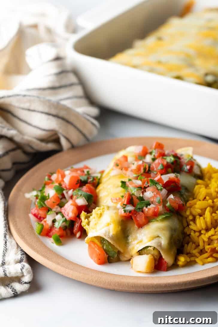 White plate with a serving of pico de gallo, two chicken enchiladas generously topped with green sauce and pico de gallo, alongside a portion of fluffy Spanish rice.