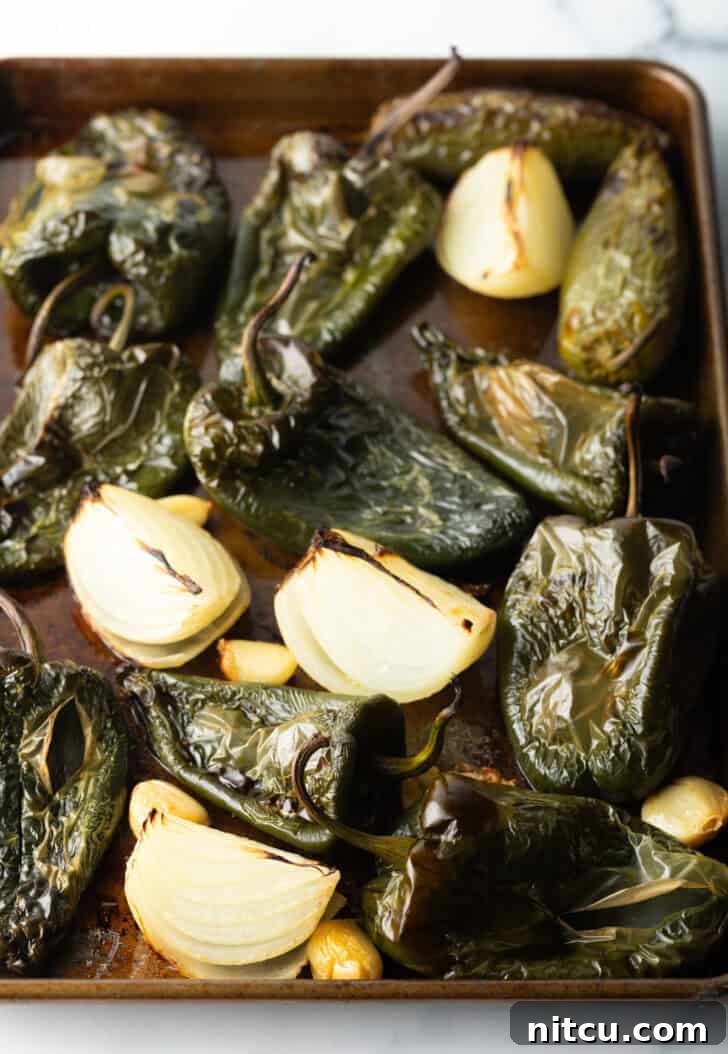 Roasted poblano peppers, caramelized onion chunks, and soft, golden garlic cloves on a baking sheet after coming out of the oven.