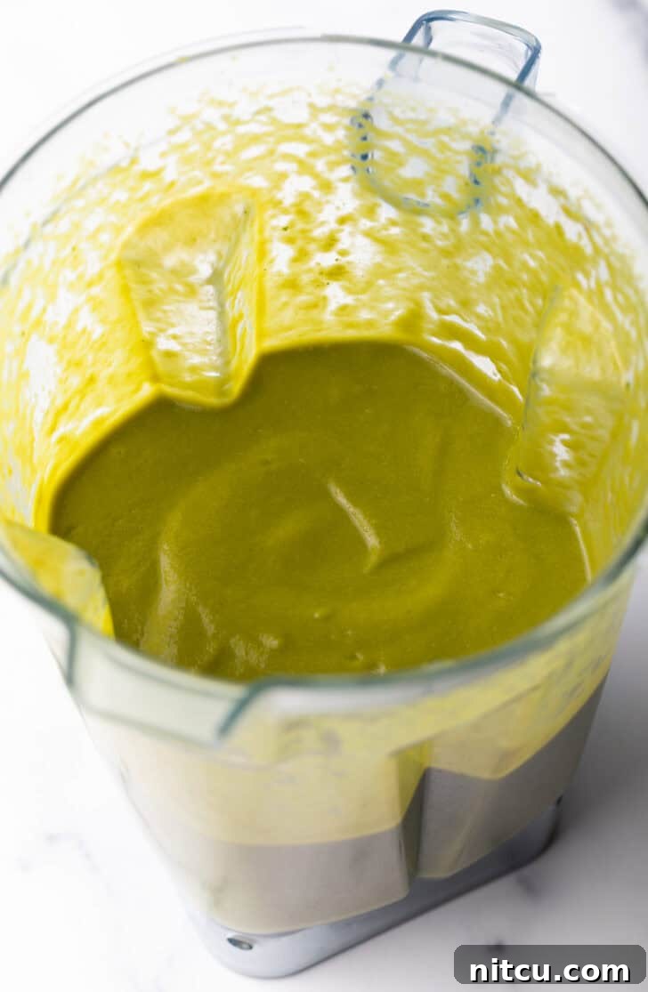 Close-up of the smooth, creamy green poblano sauce swirling inside a clear blender, ready to be poured.
