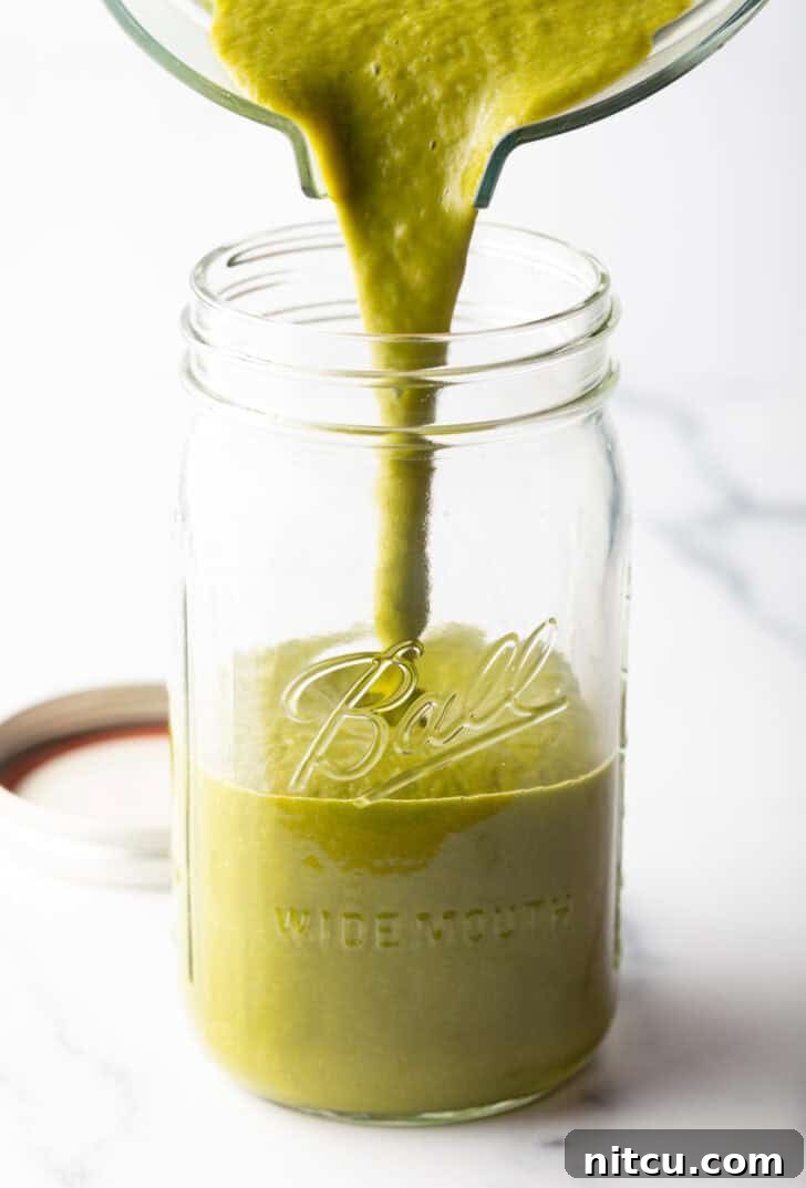 Pouring smooth green sauce from a clear blender pitcher into a large wide-mouth glass mason jar.