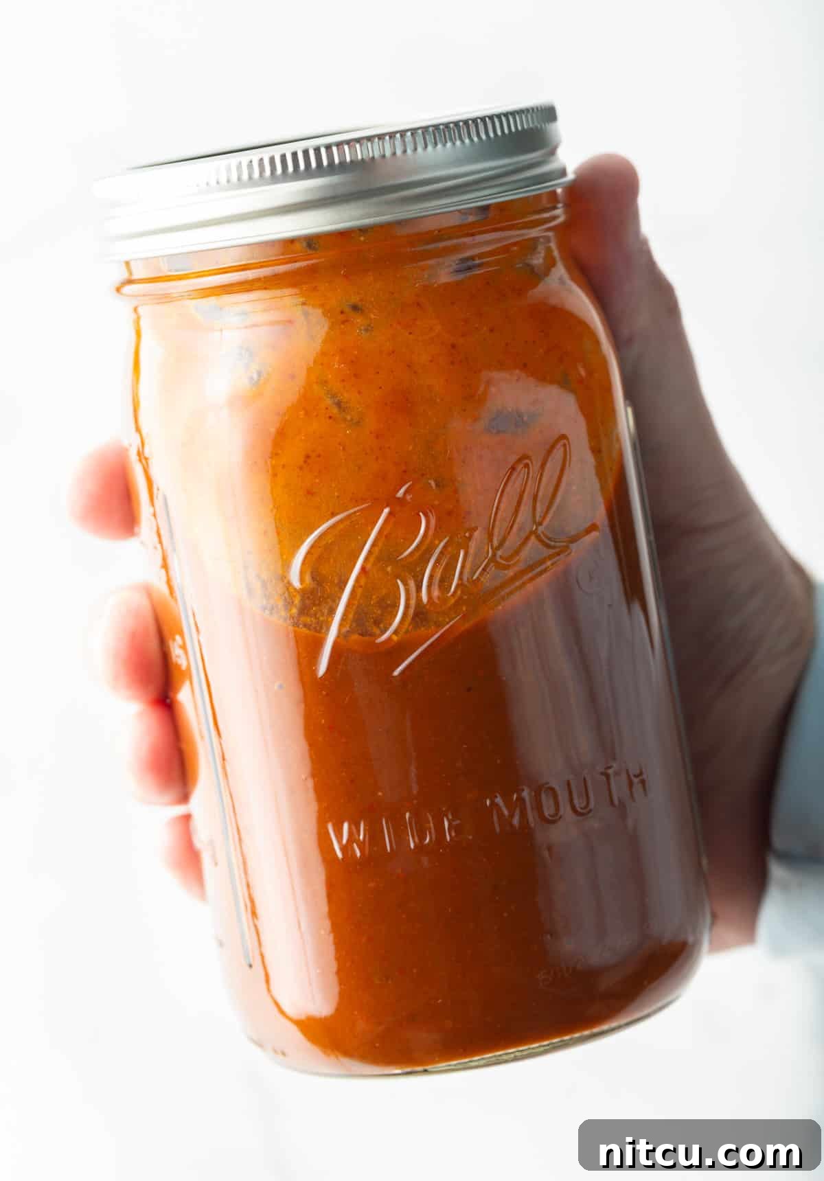 Authentic Red Enchilada Sauce 4 Hand holding a large glass mason jar filled with red enchilada sauce.