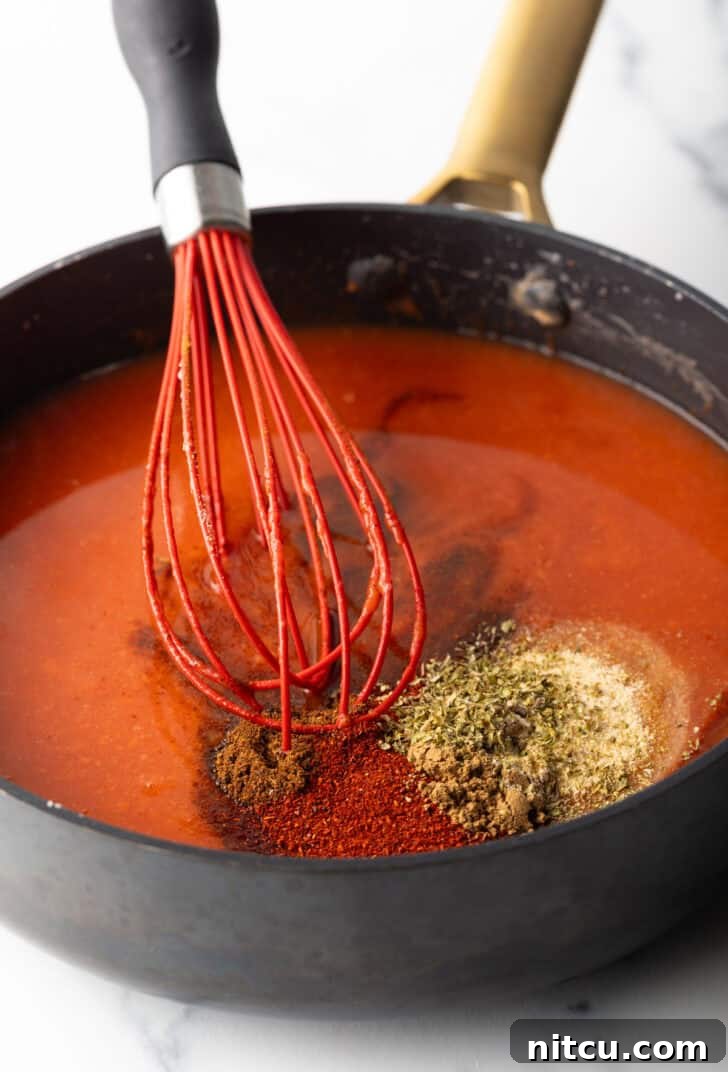 Authentic Red Enchilada Sauce 7 Large deep skillet with red sauce, spices, and a red whisk.