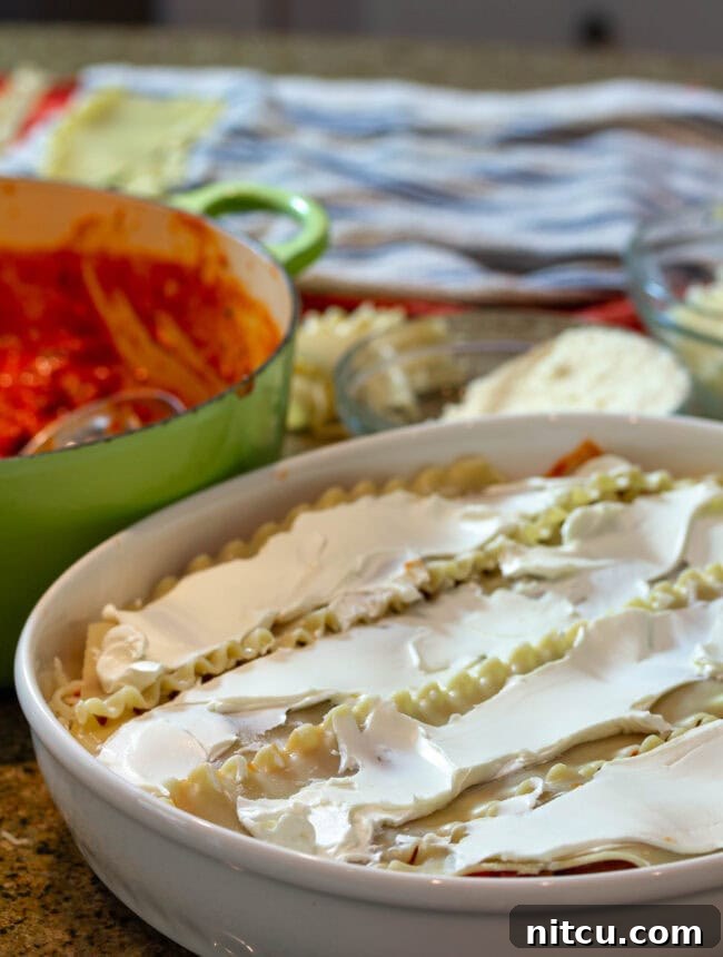 Rich Sausage Cream Cheese Lasagna 3 Chef's hands expertly layering pasta and cheese in a baking dish, forming the foundation of a delicious cream cheese lasagna.