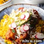 Large plate with 2 enchiladas covered in red sauce, on a pile of fluffy yellow rice and topped with fresh cabbage slaw, sliced radishes, and avocado.