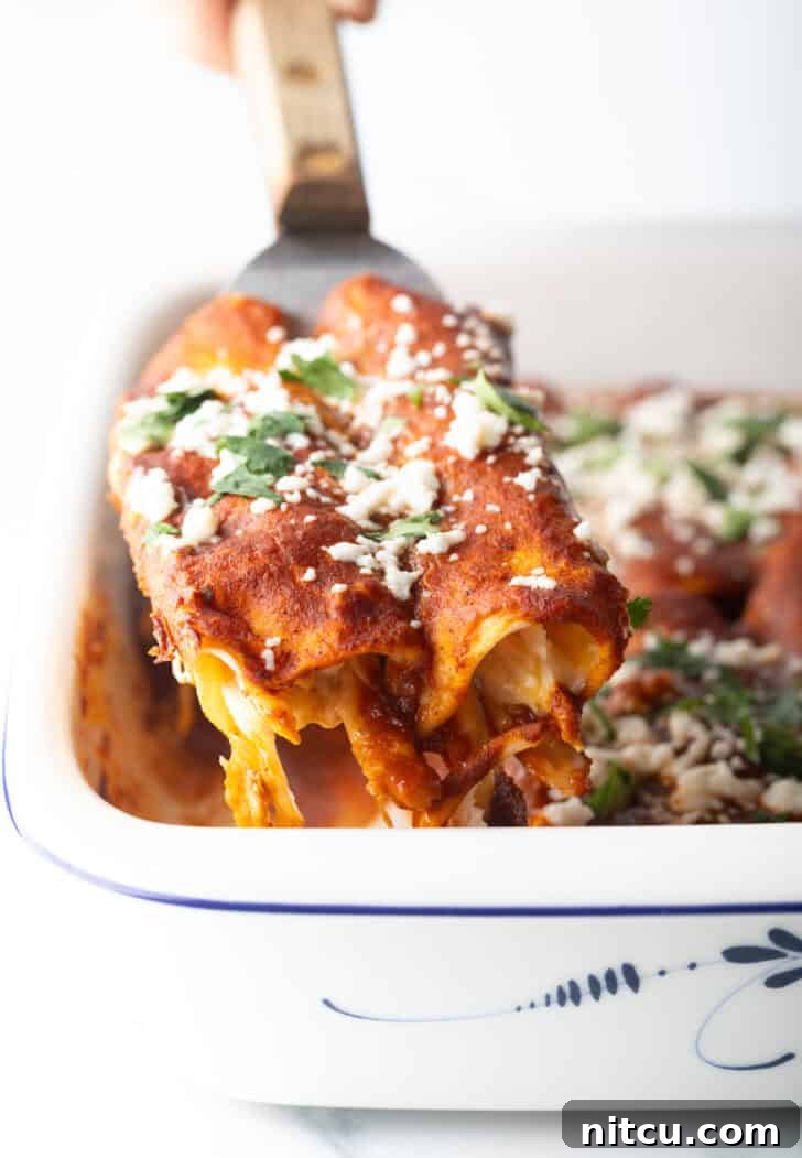 Grandma's Secret Enchiladas 5 Metal spoon lifting two enchiladas from the baking dish.