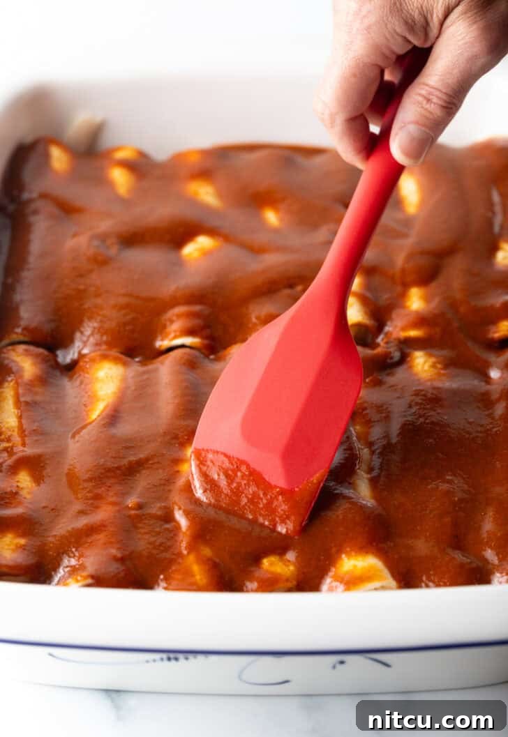 Grandma's Secret Enchiladas 9 Using a red spatula to smooth red sauce over the unbaked rolled enchiladas.