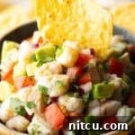 Yellow bowl of shrimp ceviche with a tortilla chip sticking in the middle.