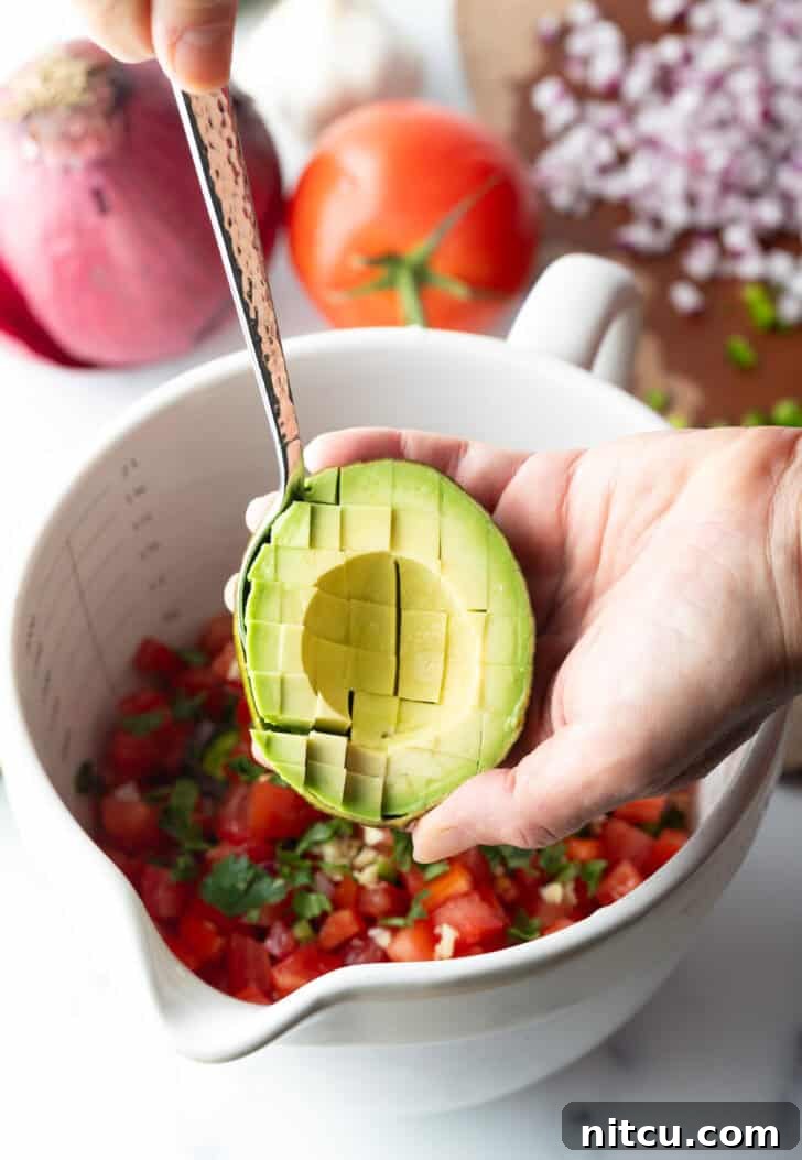 A chef's hand skillfully demonstrating how to perfectly slice half of an avocado with a sharp knife, preparing it for inclusion in the ceviche.